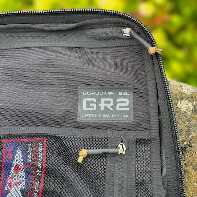 Close-up of the black GR2 26L backpack featuring mesh pockets and a visible logo patch, designed as a carry-on compliant option for convenient one-bag travel.