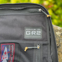 Close-up of the black GR2 26L backpack featuring mesh pockets and a visible logo patch, designed as a carry-on compliant option for convenient one-bag travel.