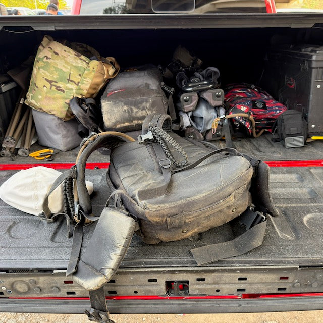 The back of a red pickup truck bed filled with several backpacks and rucking gear featuring padded hip belts.