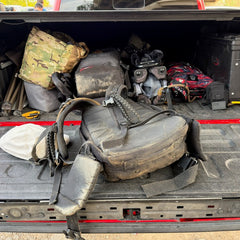 The back of a red pickup truck bed filled with several backpacks and rucking gear featuring padded hip belts.