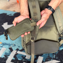 Close-up of hands attaching the Sternum / Belt Pouch - Waterproof X-PAC in olive to a backpack strap outdoors, providing hands-free storage for essential rucking gear.