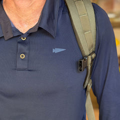 A person is wearing the Men's Long Sleeve Rucking Polo in blue, made in the USA, with a backpack strap over their shoulder.