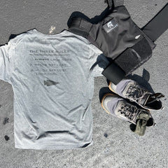 A gray Three Rules Tee - Unisex Tri-BlendX, black weighted vest, and gray sneakers are laid out on a sunny outdoor surface—gear that keeps you looking cool wherever your workout takes you.