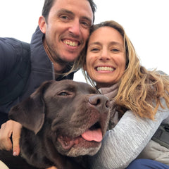 Wearing the Monster Forever Tee - PREORDER, a smiling couple hugs a happy brown dog outdoors; all three look at the camera, celebrating their joyful bond and cherishing moments that last long after crossing the Rainbow Bridge.