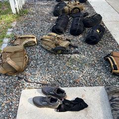 A pair of Mackall - Forged Iron + Chiseled Stone + Gum shoes with socks rest on gravel near a sidewalk, ready for any all-terrain adventure.