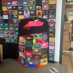 The GR1 USA backpack, made with rugged ballistic nylon and featuring a dedicated laptop compartment, is shown covered in colorful patches against a wall of similar patches.