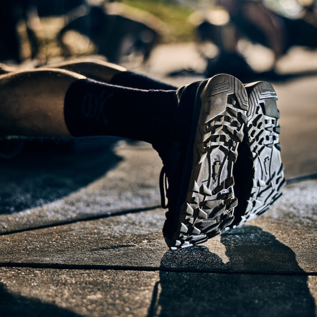 Close-up of a person’s Mackall 45 Black + Gum sneaker soles, showcasing their rugged durability as they exercise on a sunny outdoor pavement.