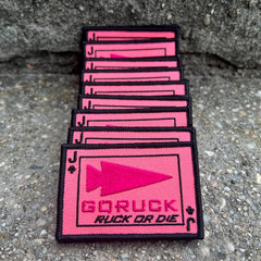A stack of rectangular, pink morale patches for a rucking challenge featuring a black arrowhead icon, a “J” club symbol, and the text “GORUCK RUCK OR DIE.”