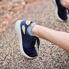 Close-up of a person's leg wearing navy and beige athletic shoes with gray ankle socks on textured outdoor ground