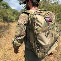 Dressed in camo, a person walks outdoors through grassy woods carrying the GR1 USA - Ballistic Nylon Cordura (The Original Ruck) everyday rucksack.