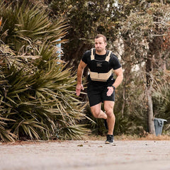 Athletic man running outdoors wearing GORUCK weighted vest training on a trail surrounded by trees
