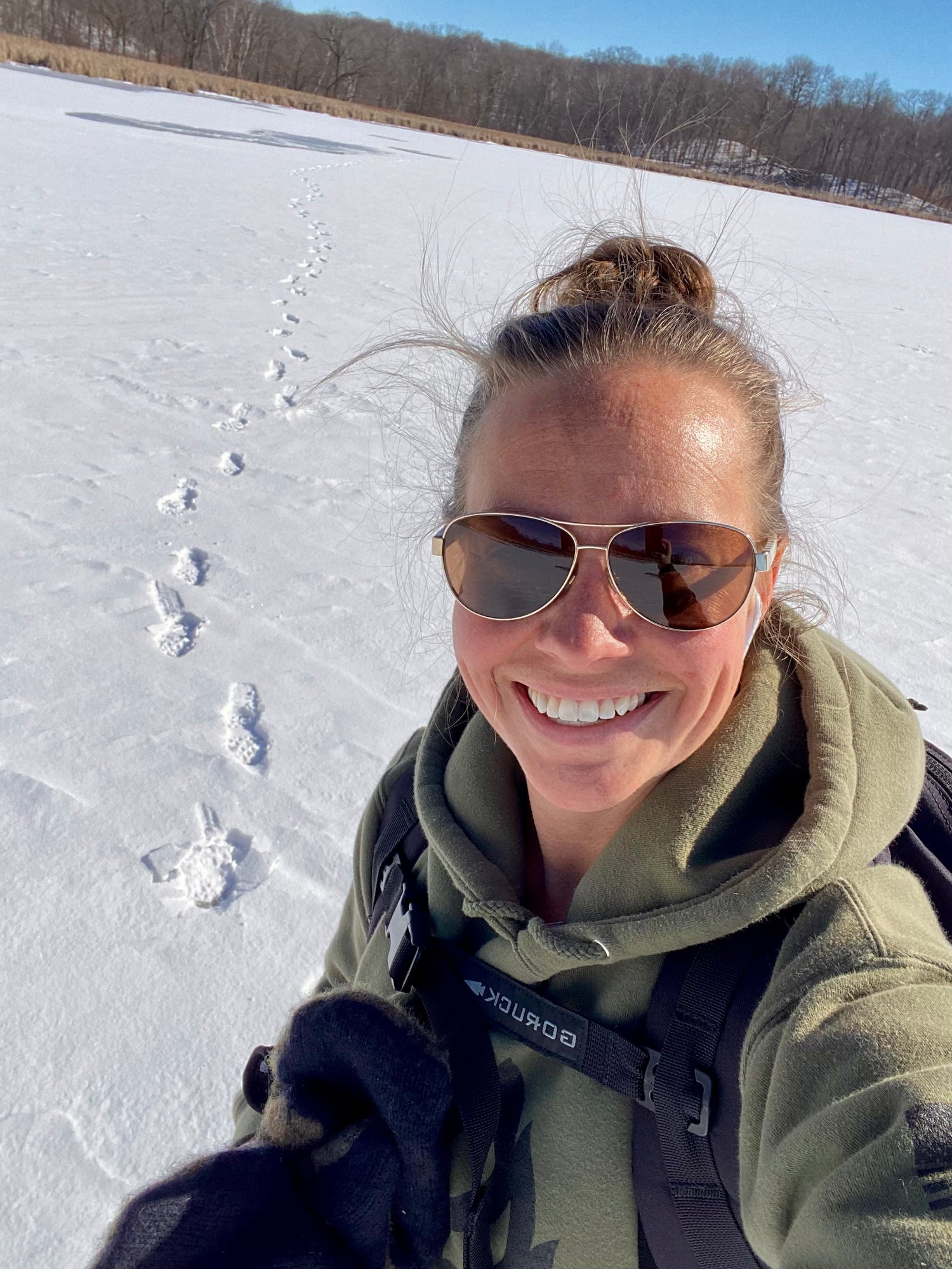 Smiling woman in sunglasses stands on a snowy field with footprints behind her, under a clear blue sky—proudly taking on the Patch - Ruck Fit Challenge to Start 2026 Strong.