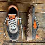 Two Mackall 45 Fog sneakers in gray, brown, and orange with arrow logos shown on a worn wooden surface.