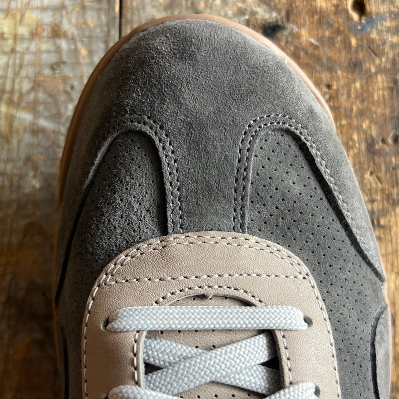 Close-up of the Mackall 45 Fog sneaker in gray suede with white laces, displayed on a worn wooden surface.