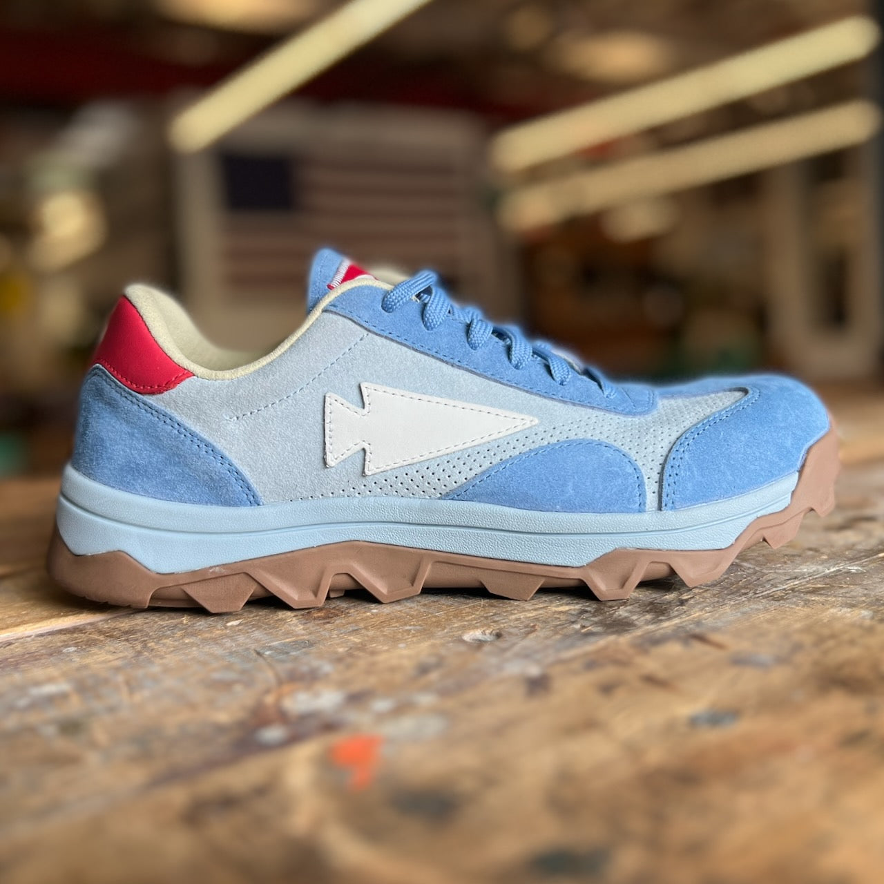 Mackall 45 Americana sneaker in blue suede, featuring a white zigzag logo, red heel patch, and tan rugged sole, displayed on a wooden surface.