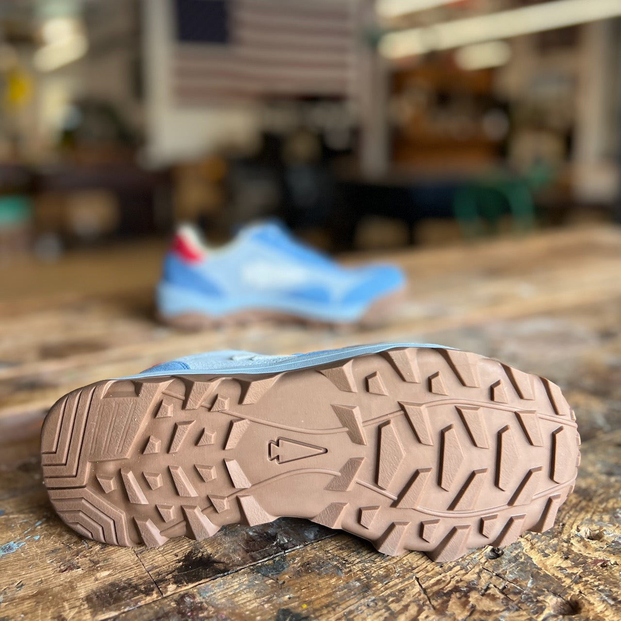 Close-up of the Mackall 45 Americana’s rugged sole on a wooden surface, with another shoe and a blurred flag visible in the background.