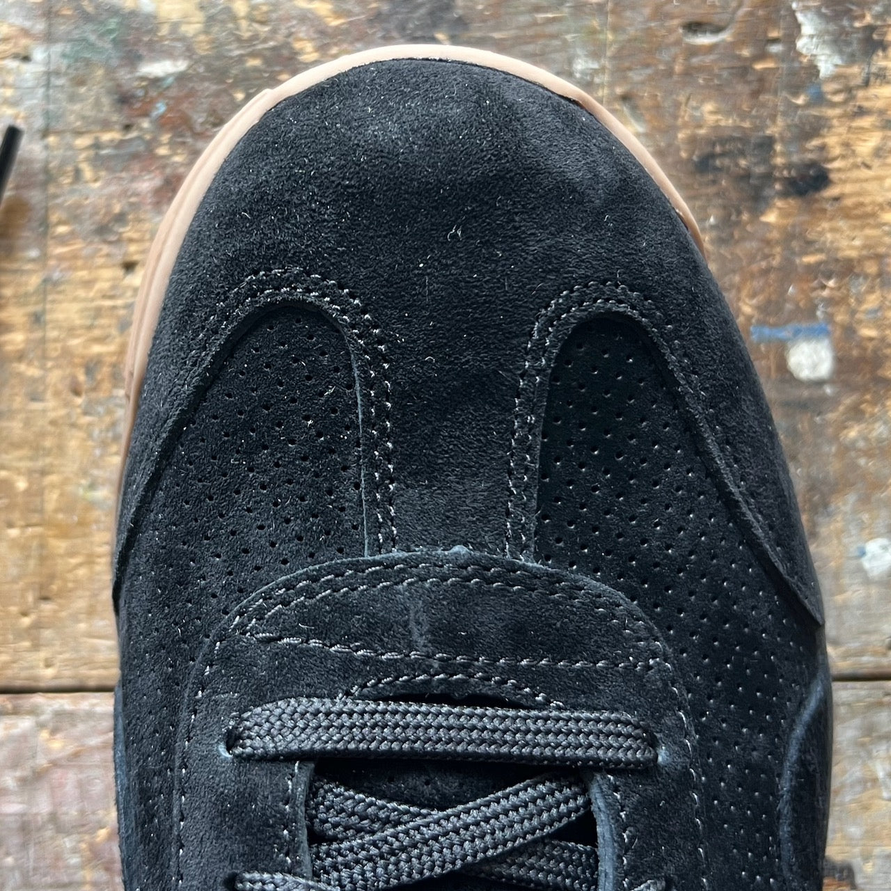 Mackall 45 Black + Gum sneaker with black laces on a worn wooden surface, seen from above.