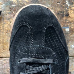 Mackall 45 Black + Gum sneaker with black laces on a worn wooden surface, seen from above.