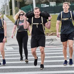 Four active adults rucking outdoors on a street crosswalk wearing GORUCK backpacks and athletic gear