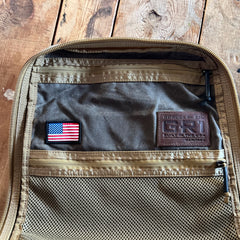 Open brown GR1 USA - Heritage Waxed Canvas rucksack with a mesh pocket, American flag patch, and an interior leather “GORUCK GR1” label—crafted from durable waxed duck canvas for a classic heritage look.