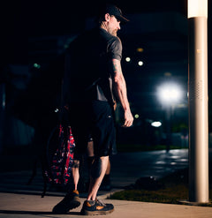 Man in shorts and cap walking at night under streetlights, carrying a duffel bag fitted with the rugged Mackall 45 Fog rucking chassis.