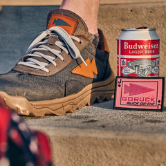 A sneaker with orange arrow accents, a can of Budweiser, and a GORUCK patch on concrete steps during an Austin rucking event.