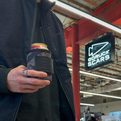 A person holds a canned drink in a Ballistic Beer Jacket - GORUCK, standing indoors near a GORUCK SCARS sign.
