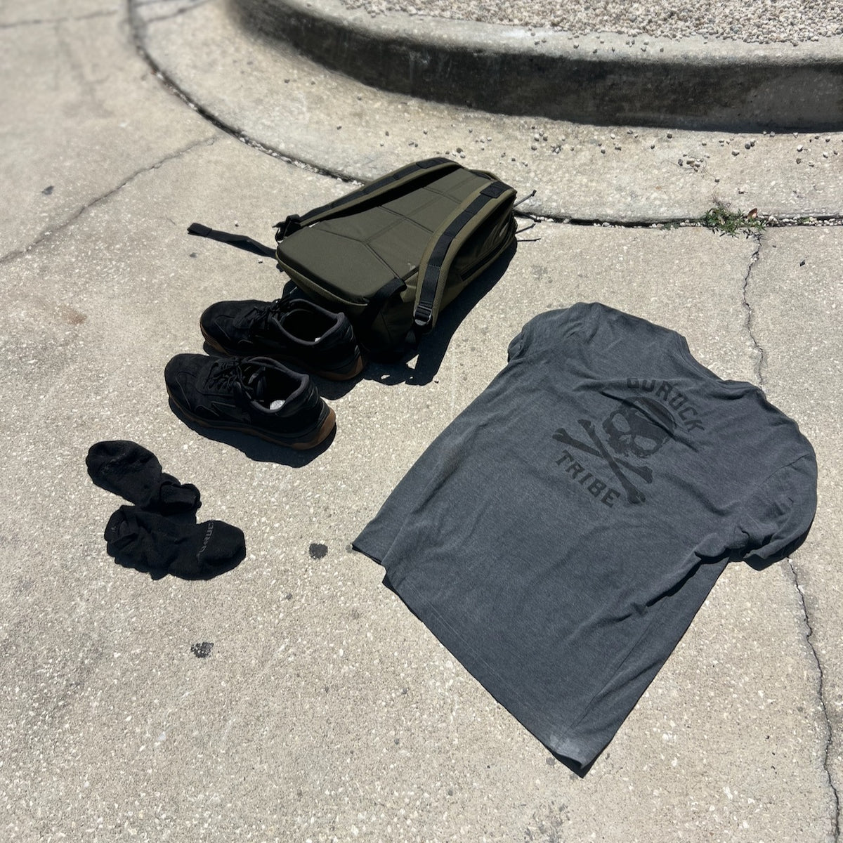 GORUCK Tribe Tee - Tri-Blend, shoes, socks, and a bag are laid out on sunlit concrete near a curb—a simple scene that captures the spirit of real community inspired by the GORUCK Tribe.