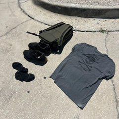 GORUCK Tribe Tee - Tri-Blend, shoes, socks, and a bag are laid out on sunlit concrete near a curb—a simple scene that captures the spirit of real community inspired by the GORUCK Tribe.