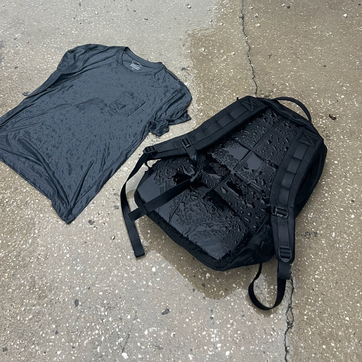 A wet gray t-shirt and a comfortable rucksack lying on a damp concrete surface after a distance rucking event.