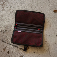A Scars Wire Dopp pouch, made of waxed twill in red and black with mesh pockets, is open on a concrete surface.