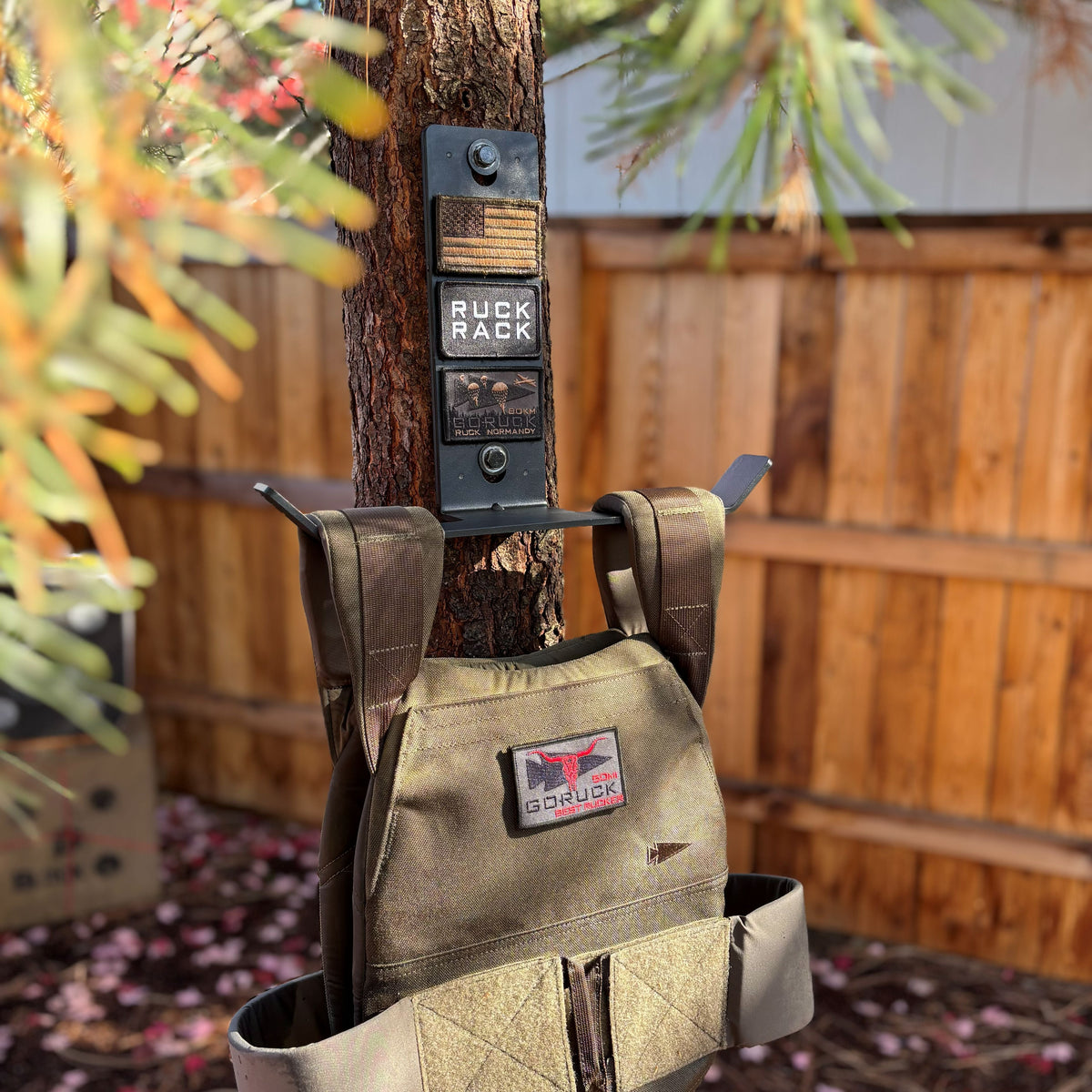 A GORUCK plate carrier hanging on a Ruck Rack Monster mount attached to a tree trunk for tactical gear storage.