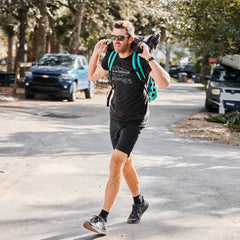 A man in athletic wear enjoys a sunny outdoor walk carrying a weighted sandbag, wearing Merino Challenge Socks - Trail Cuff for lasting comfort and durability.