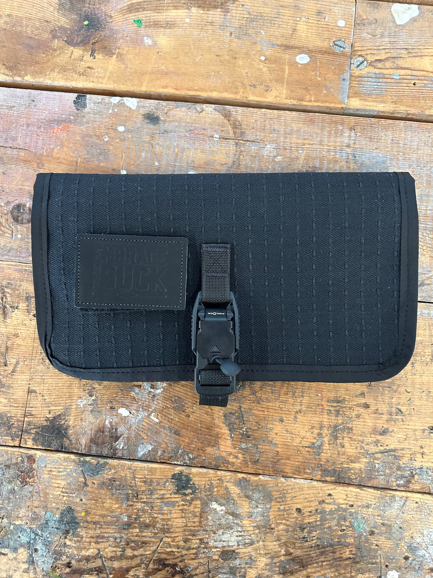 The Scars Wire Dopp, a black EDC cable organizer with zip and buckle, is displayed on a worn wooden surface.