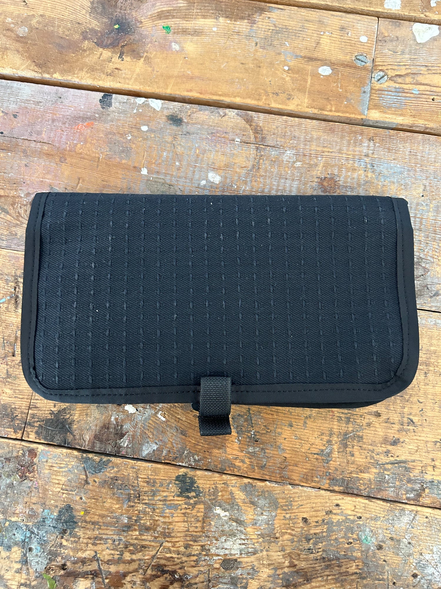 The Scars Wire Dopp is a black, rectangular Japanese Denim pouch with a flap, shown on a worn wooden surface—perfect as an EDC cable organizer.