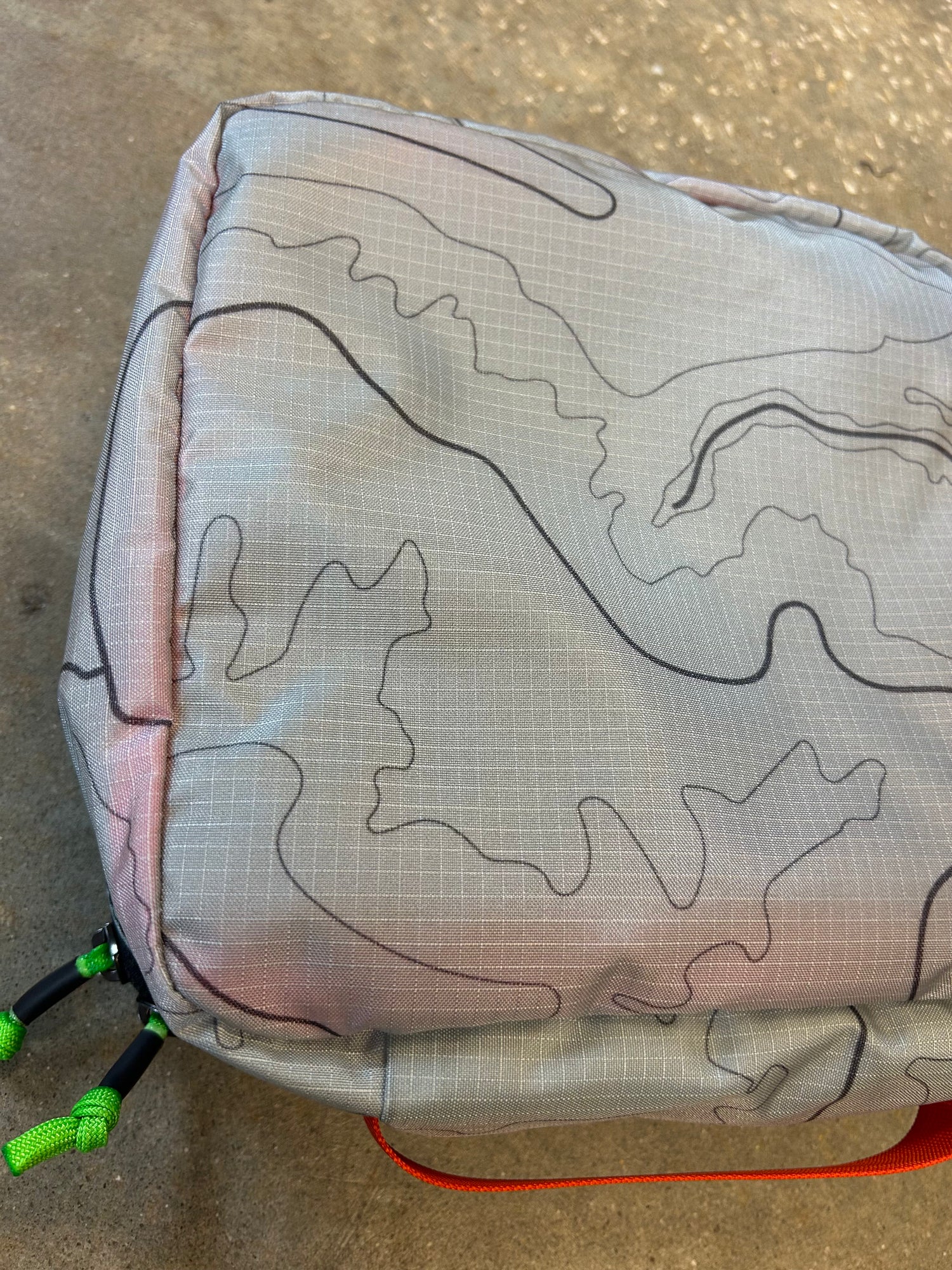 Close-up of the Ripstop Robic XL Packing Cube in gray with black contour lines and green zipper pulls, ideal for travel organization, displayed on a textured surface.