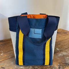 The Scars Tote is a durable blue grocery bag with yellow stripes, navy handles, mesh sides, and an orange interior—perfect as your everyday tote bag.