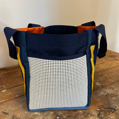 The Scars Tote, made from blue and orange 1000D Cordura with a white mesh front panel, rests on a wooden surface—perfect for everyday use.