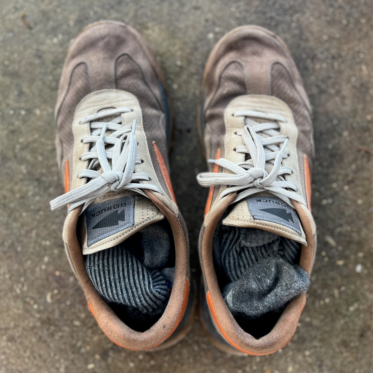 A pair of Mackall 45 Fog sneakers with socks tucked inside, placed on a rough concrete surface.