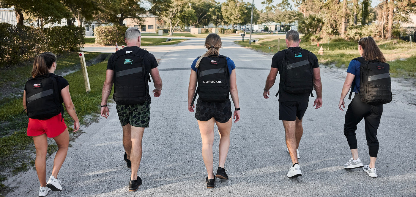 Five people carrying Ruck Bundle backpacks walk down a sunlit street, seen from behind.