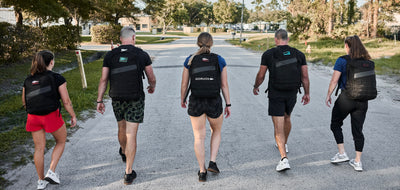 Five people carrying Ruck Bundle backpacks walk down a sunlit street, seen from behind.