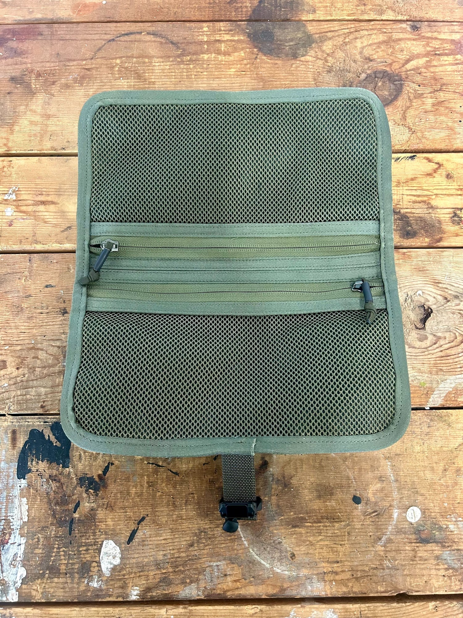 A Scars Wire Dopp, featuring open green mesh, lies flat on a worn wooden surface.