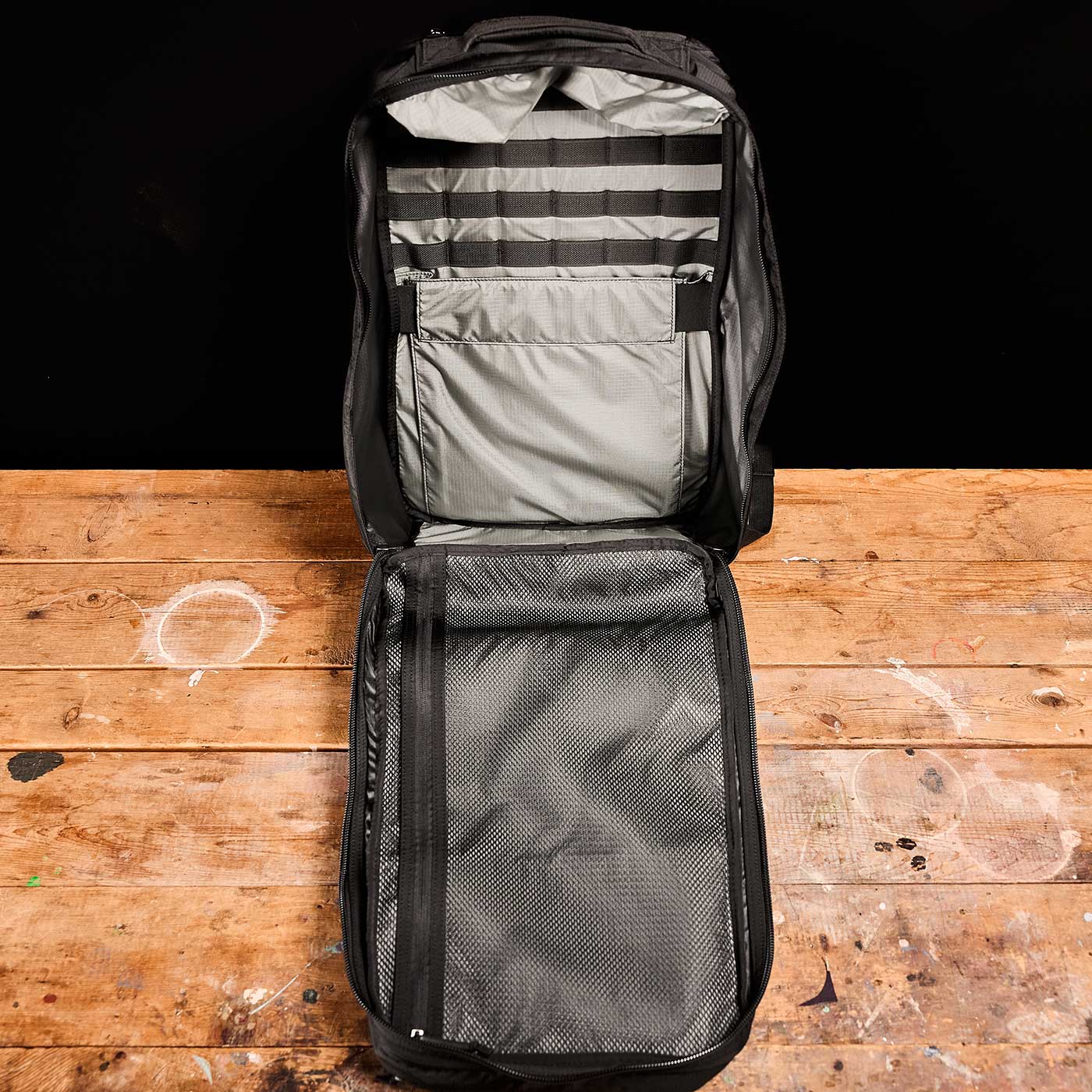 Open black backpack with organized inner compartments, lying on a wooden surface against a black background.