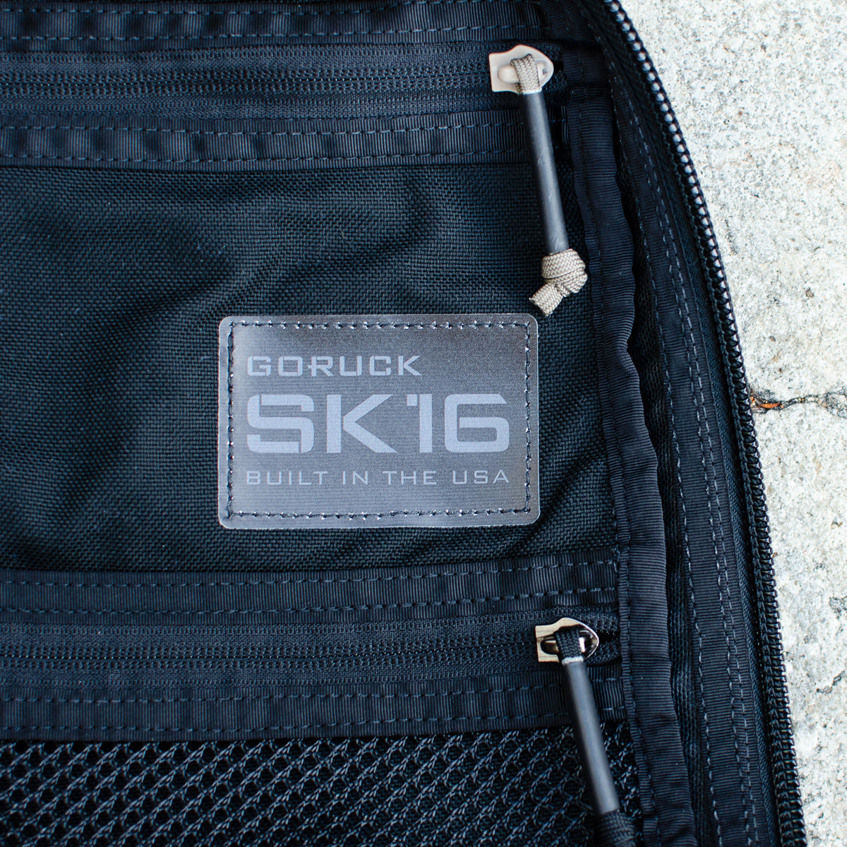 Close-up of a GR0 USA Slick - Ballistic Nylon Cordura tag on a black mesh pocket with zippers, made in the USA from rugged Cordura for top-tier durability.