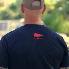 Back view of a person wearing a navy GORUCK t-shirt with red logo, outdoors in daylight