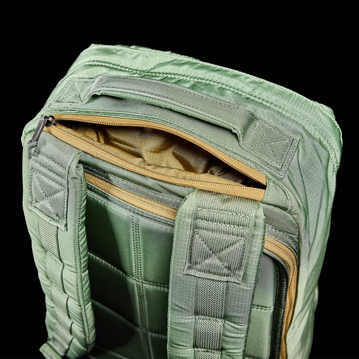 Close-up of a GR1 USA - Ripstop ROBIC® rucksack by GORUCK in green against a black background. The top zipper compartment is open, showcasing its tan interior. This water-resistant bag boasts cushioned straps and reinforced stitching with a quilted texture.
