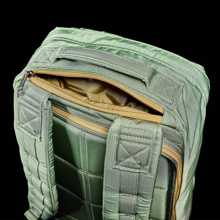 Close-up of a GR1 USA - Ripstop ROBIC® rucksack by GORUCK in green against a black background. The top zipper compartment is open, showcasing its tan interior. This water-resistant bag boasts cushioned straps and reinforced stitching with a quilted texture.
