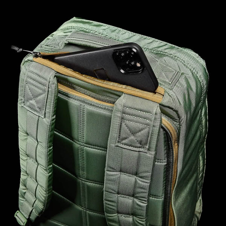 Introducing the GORUCK GR1 USA - Ripstop ROBIC®: This green tactical rucksack features padded straps and a quilted design, crafted from water-resistant material to withstand any adventure. The partially unzipped top compartment reveals a black smartphone nestled inside. The sleek black background highlights the backpack's exquisite texture and details.