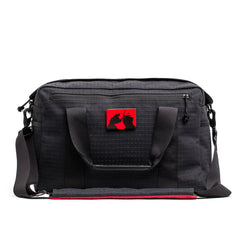Black GORUCK duffel bag with textured fabric, dual handles, shoulder strap, and red patch featuring samurai silhouettes