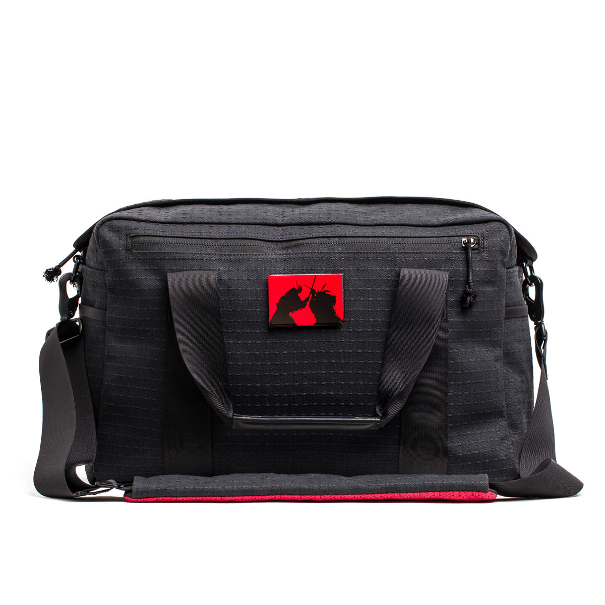 The Kit Bag x Carryology - GRXC2 Samurai 2.0 is a black duffel with handles, a shoulder strap, and a red patch with two black unicorns—crafted from custom technical fabric and inspired by the iconic Samurai Kit Bag design.